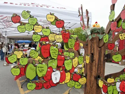 Hundreds of messages are left on apple shaped paper and attached to a wooden tree structure.